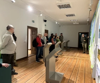 Grupa przewodników podczas szkolenia w Muzeum SPN w Czołpinie. Uczestnicy skupieni wokół mapy parku, słuchający pracownika w sali muzealnej.